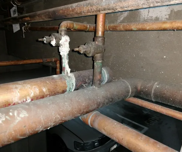 Copper plumbing pipes in a crawl space showing significant corrosion and white mineral buildup around the joints.