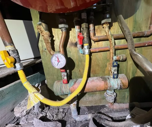 A section of copper plumbing featuring heavy limescale buildup and crusting around the threaded connections and valves.