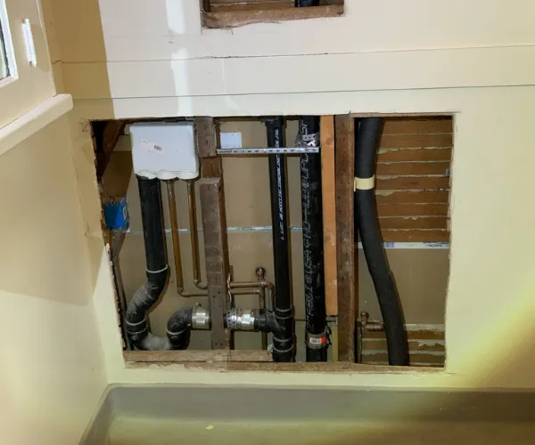 Close-up of a corroded copper pipe joint with significant white mineral deposits and green oxidation in a dark utility space.