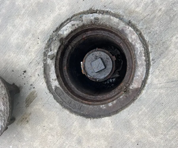 Close-up of a corroded copper pipe joint with significant white mineral crust and green oxidation in a dark utility space.